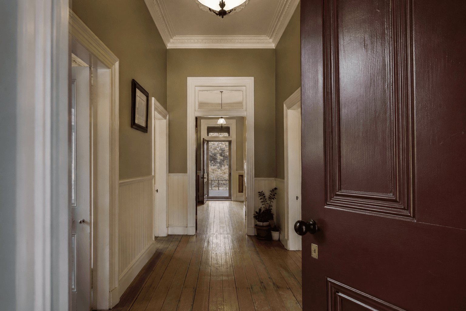 Heritage hallway with cream walls, detailed timber trim and a burgundy front door